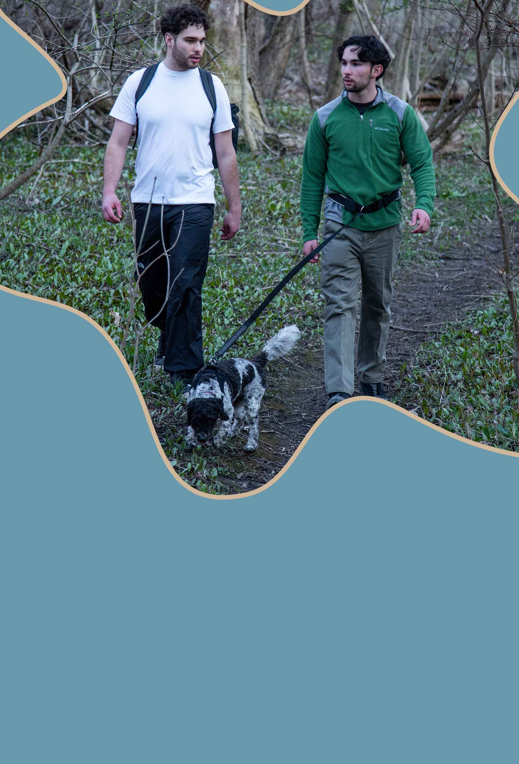 Two men hiking a forest trail with a dog using a black hands-free dog leash for safe and comfortable outdoor walking.