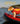 Small dog wearing a bright orange and yellow life jacket standing on a red canoe, ready for safe water activities and swimming.
