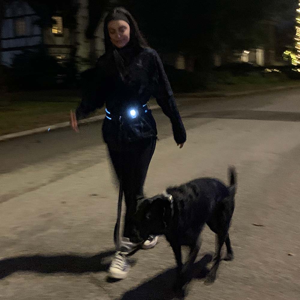 Woman jogging with her dog using a hands-free leash and light-up running belt at night for safe and visible outdoor exercise.